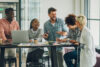 A diverse group of people standing around a table having a meeting and laughing.